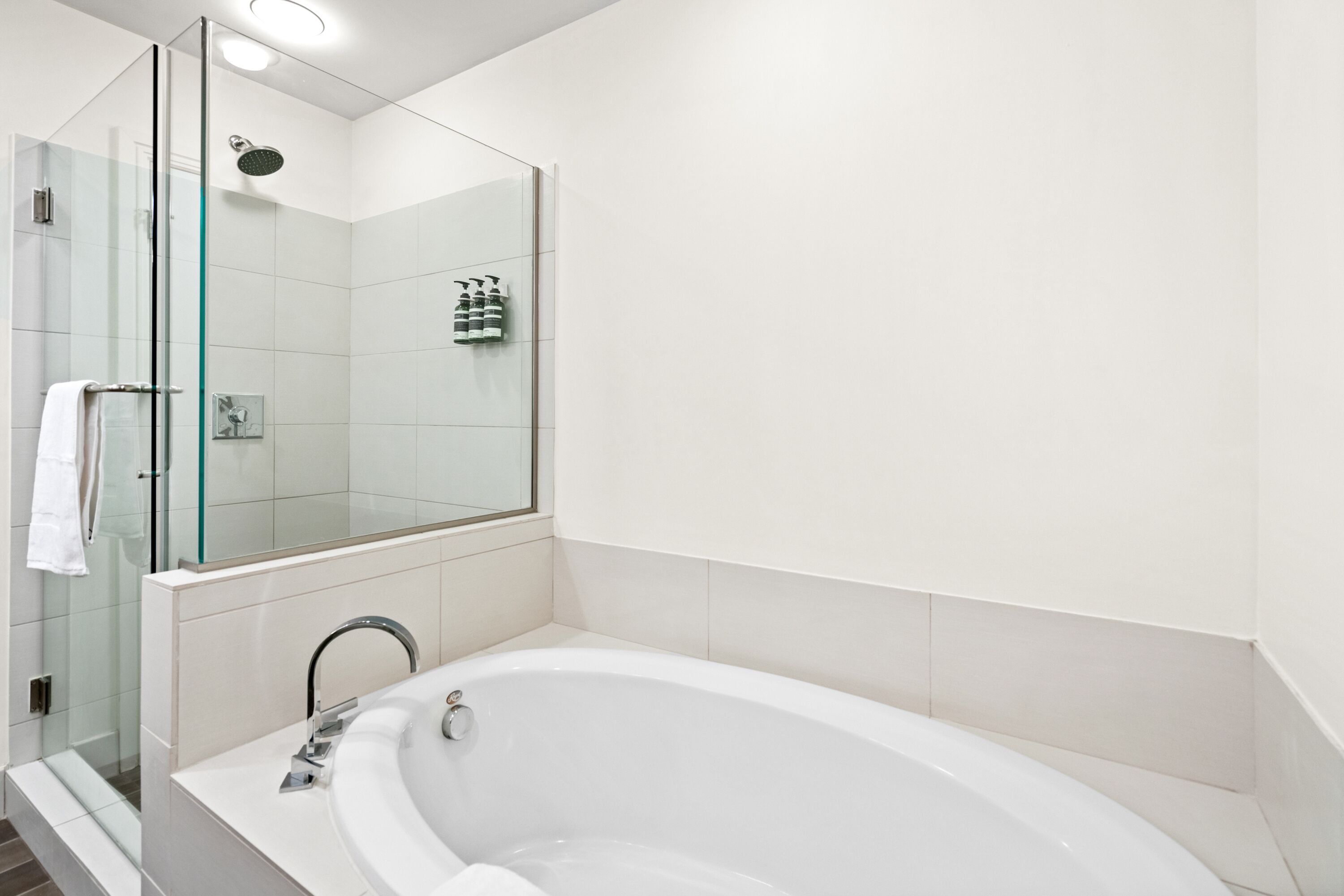 Un baño moderno con ducha envuelta en vidrio, una bañera blanca y un espejo grande.
