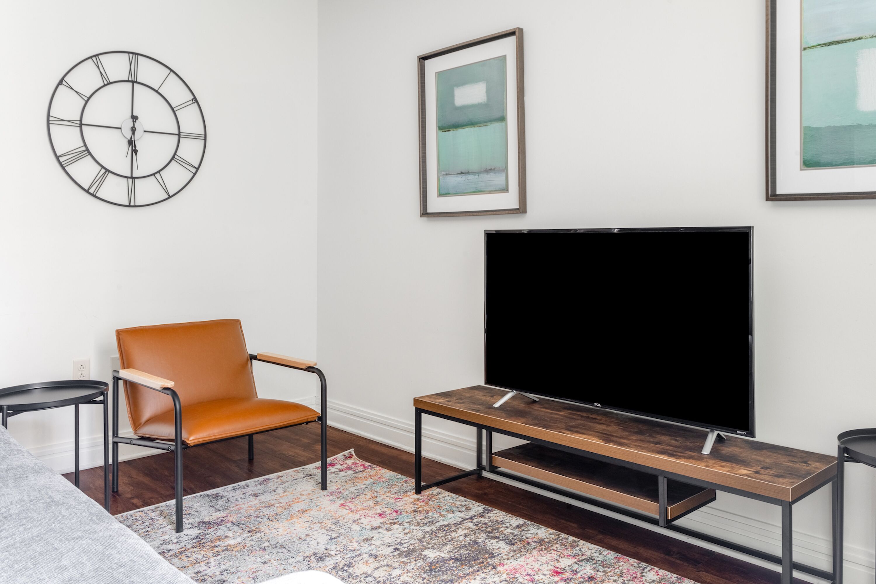 Una sala de estar con un televisor de pantalla plana grande, una silla moderna, una mesa de centro y un reloj de pared.
