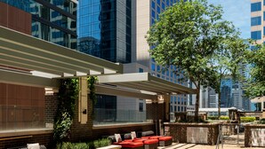 Una piscina en la azotea con asientos rojo y beige, rodeada de edificios modernos y un árbol.