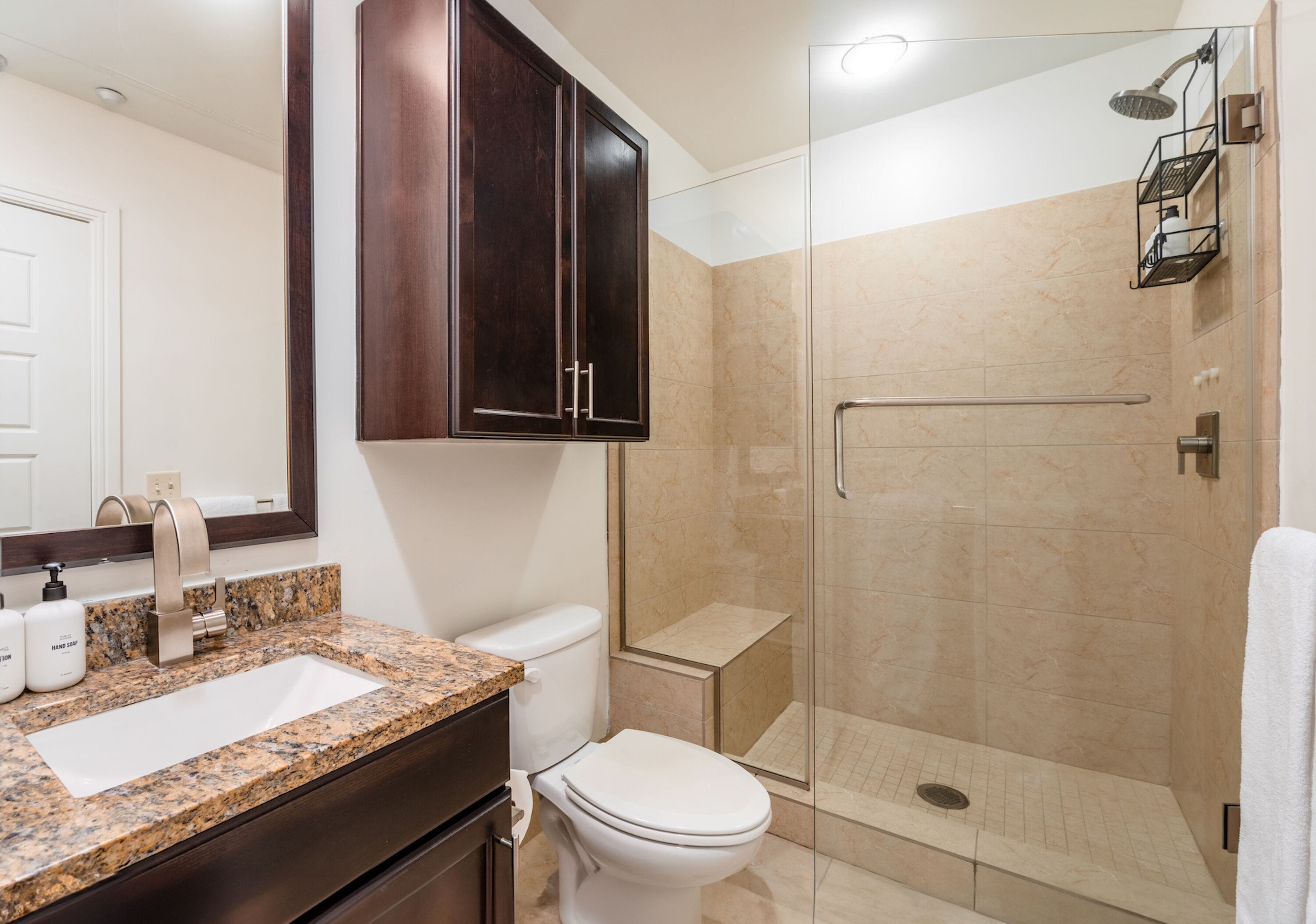 A bathroom with a marble sink, dark wooden cabinets, a white toilet, and a glass-enclosed shower area.