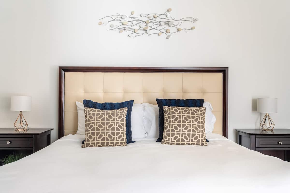 A neatly made bed with a tufted headboard, two patterned pillows, and a decorative wall piece above.
