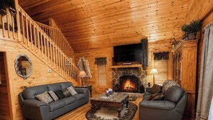 A log cabin interior with a fireplace, two sofas, a coffee table, and a staircase. - Deer Run, Free Attraction Tickets, Hot Tub, Resort Playground, Near Dollywood!!! (Sevierville)