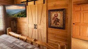 A wooden interior with a bed, a mounted TV, a sliding barn door, and a framed picture. - Deer Run, Free Attraction Tickets, Hot Tub, Resort Playground, Near Dollywood!!! (Sevierville)