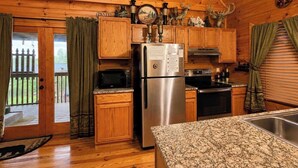 A cabin kitchen with wooden walls, a stainless steel refrigerator, a microwave, and a stove. - Deer Run, Free Attraction Tickets, Hot Tub, Resort Playground, Near Dollywood!!! (Sevierville)