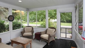A sunroom with wicker chairs, a dartboard, and a wooden table. - Charming 4 Bedroom Farmhouse in Saugatuck, perfect for a family getaway! (Saugatuck)