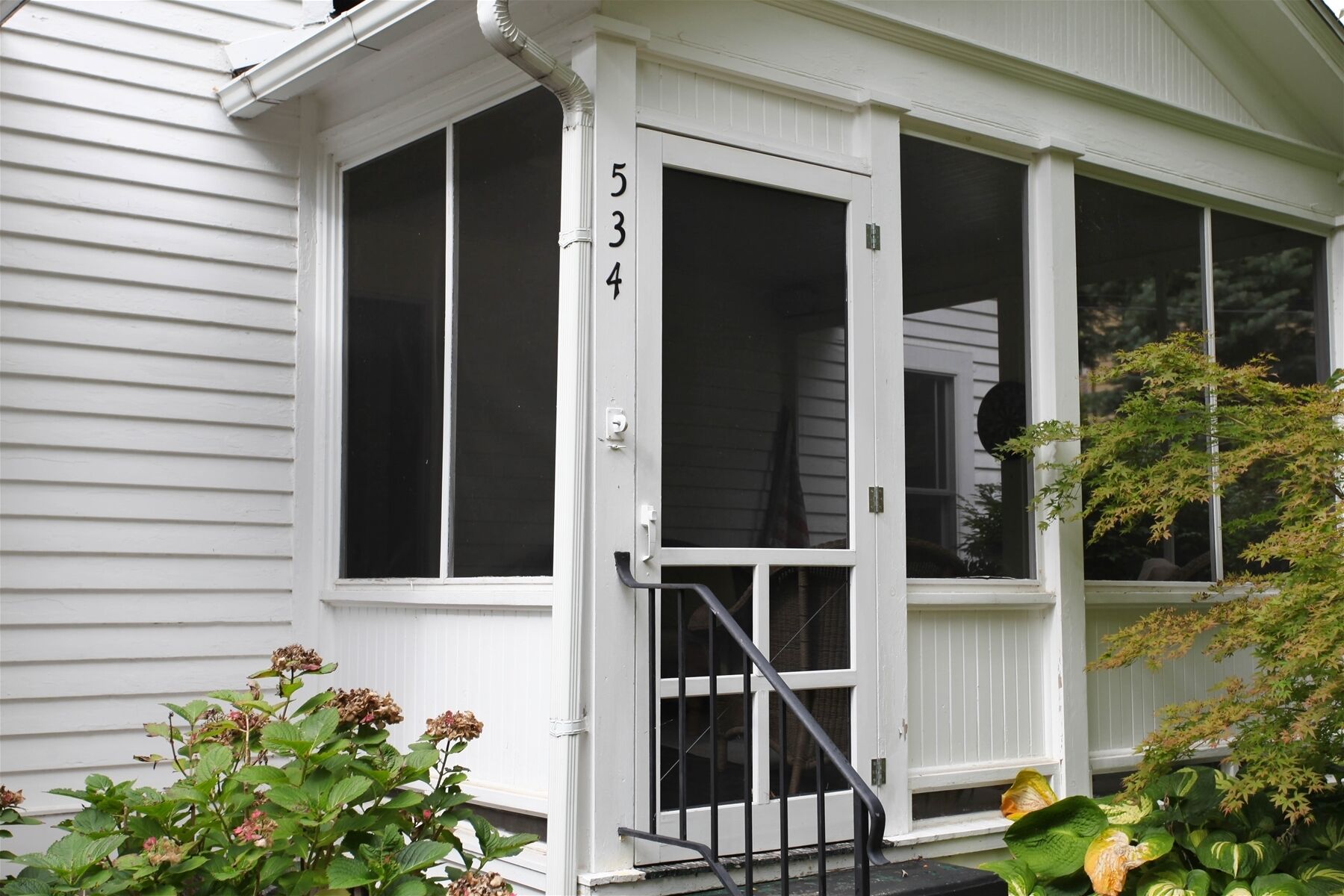 A white house with a number '534' on the door, a covered porch, and a small garden with plants.