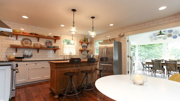 A modern kitchen with wooden cabinets, a stainless steel refrigerator, and a bar area with stools. - Charming 4 Bedroom Farmhouse in Saugatuck, perfect for a family getaway! (Saugatuck)