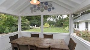 A covered patio with a table and chairs, a hanging light fixture, and decorative plates on the wall. - Charming 4 Bedroom Farmhouse in Saugatuck, perfect for a family getaway! (Saugatuck)