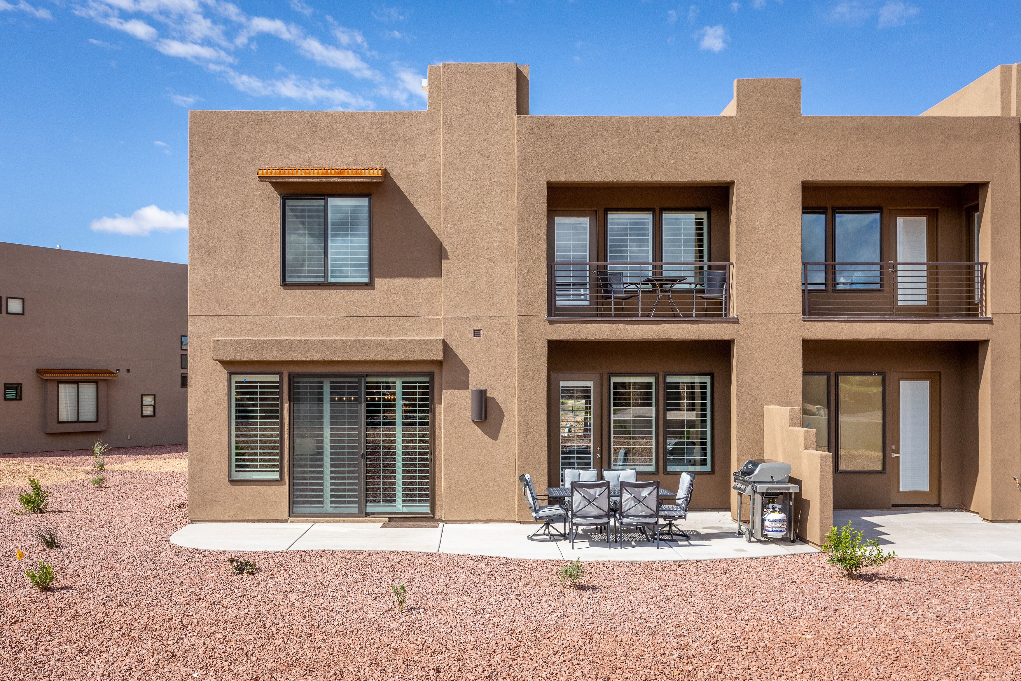 A modern two-story building with a flat roof, large windows, and a patio area with outdoor furniture.