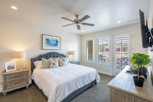 A bedroom with a bed, nightstands, a ceiling fan, a window with blinds, and a potted plant.