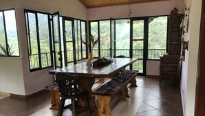 Un espace repas avec une table en bois, des bancs et de grandes fenêtres donnant sur l’extérieur.