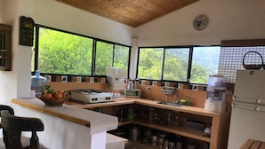 Une cuisine équipée d’une cuisinière à gaz, d’un évier et d’un réfrigérateur. Des fenêtres offrent une vue sur la verdure environnante.