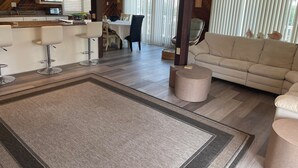 Eine moderne Küche mit weißen Schränken, einer Mikrowelle und einem Backofen. Es gibt einen Essbereich mit Tisch und Stühlen sowie ein Wohnzimmer mit Sofa und Couchtisch.