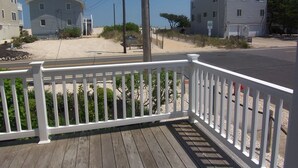 Eine Holzterrasse mit weißen Geländern, ein Sandstrand und Häuser im Hintergrund.
