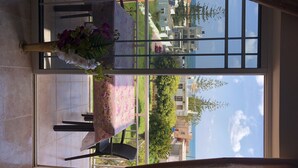 A balcony with a table set for two, a vase of flowers, and a view of the cityscape through a window. - Welcome to SEASIDE APARTMENT (agia marina)