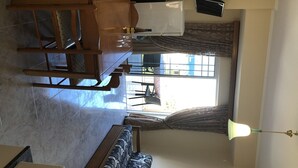 A dining area with a wooden table and chairs, a window with curtains, and a ceiling fan. - Welcome to SEASIDE APARTMENT (agia marina)
