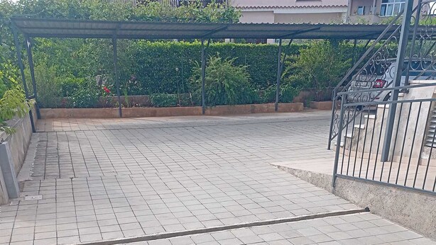 A paved outdoor area with a metal railing, a concrete bench, and a metal pole.