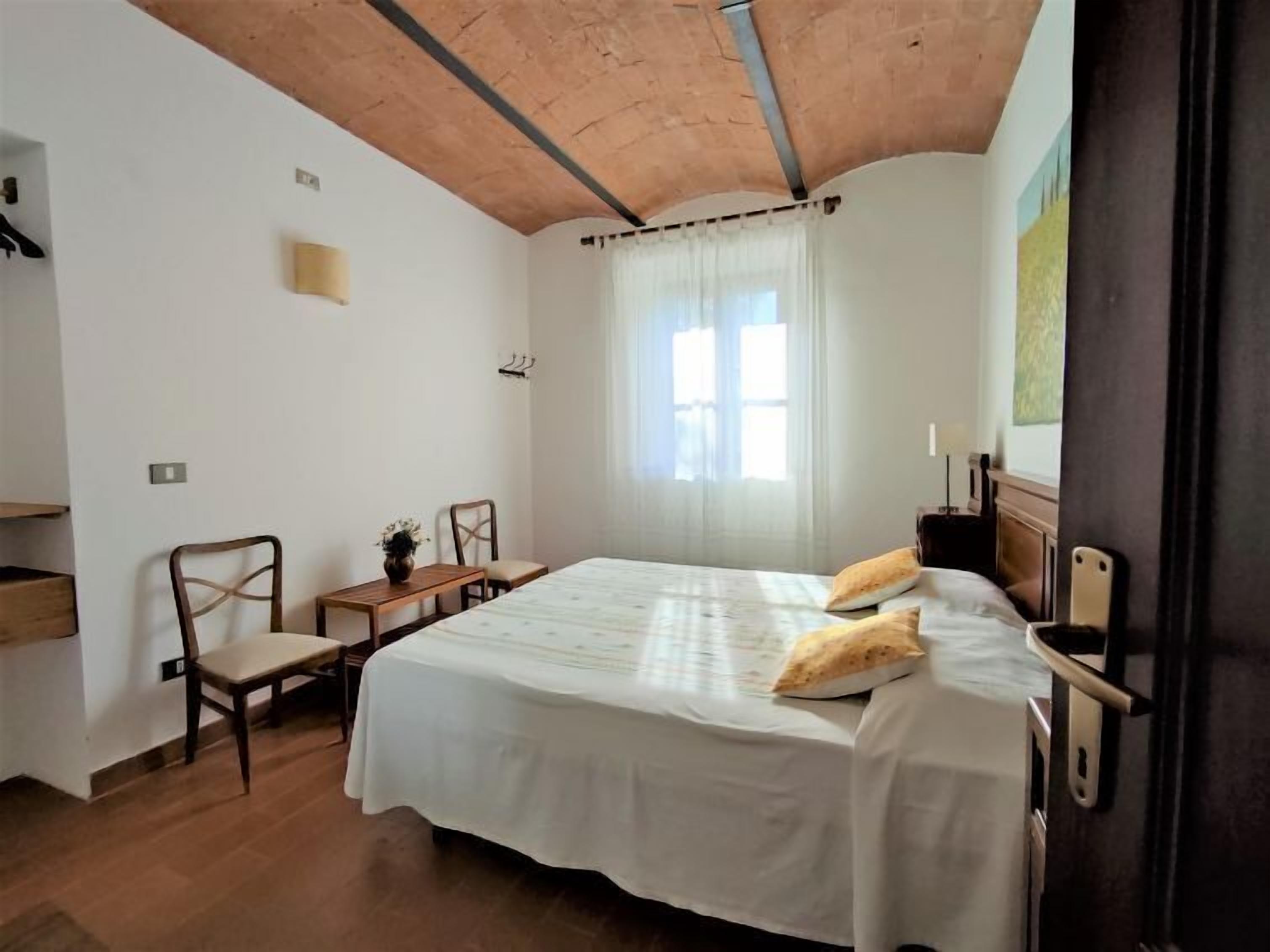 A bedroom with a large bed, a wooden desk, a chair, and a window with curtains.