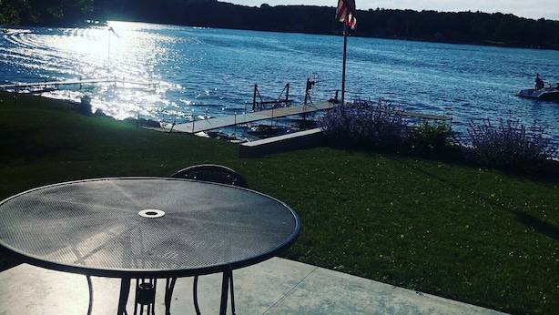 A lakeside patio with a metal table and chairs, a dock with a boat, and an American flag. - Quiet Lakefront property on Cassadaga Lake WiFi & 2 car parking. (Cassadaga)