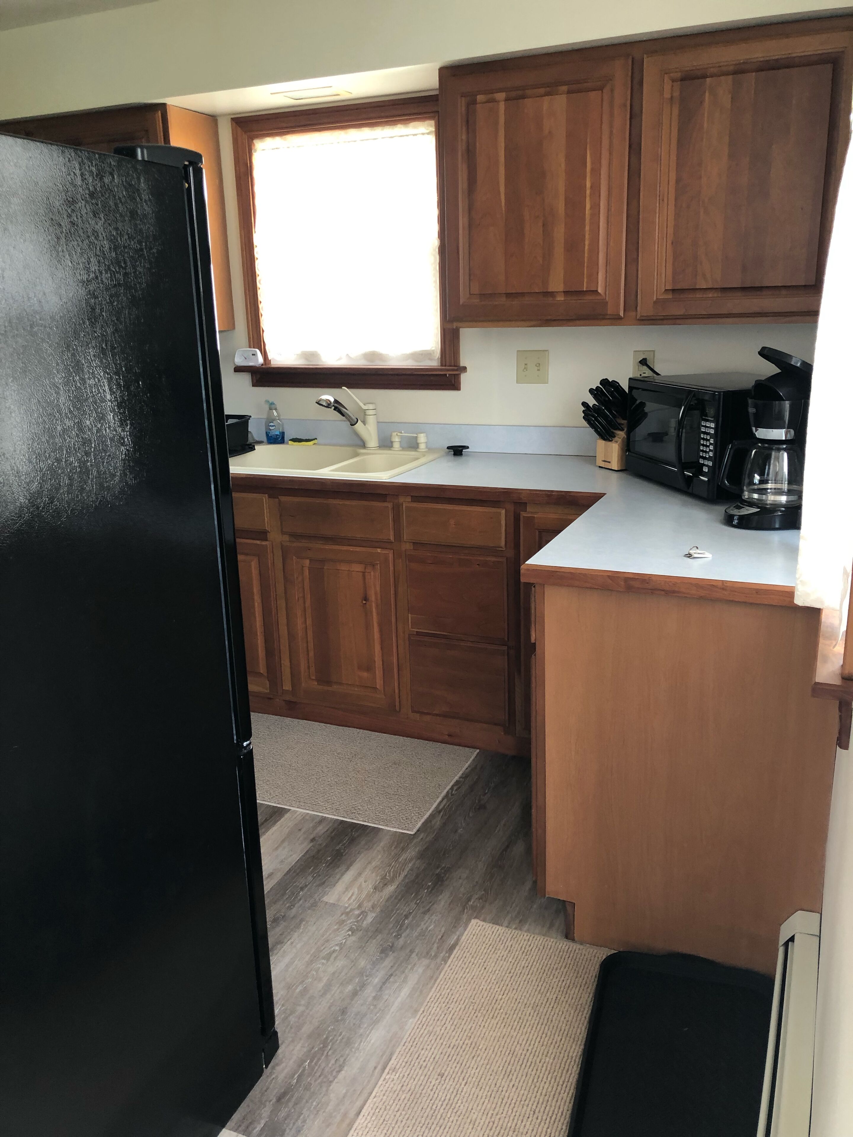 Eine kleine Küche mit Holzausstattung, einem schwarzen Kühlschrank, einer Spüle, einer Mikrowelle und einer Kaffeemaschine.
