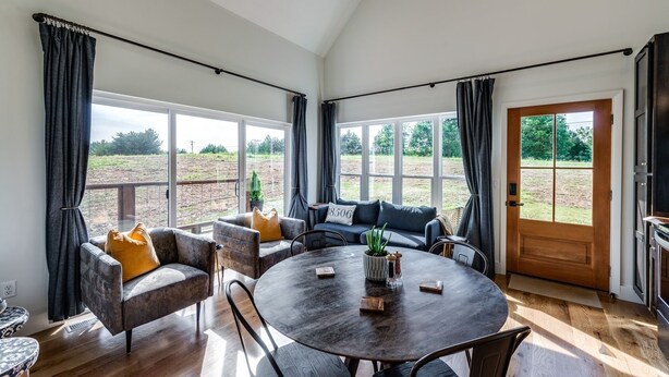 A spacious living room with a round table, two sofas, and a large window offering a view of the outdoors.