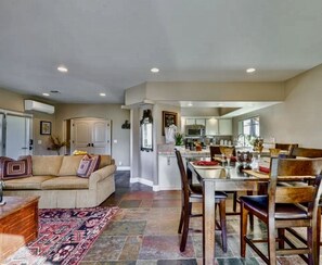 A spacious living area with a sofa, coffee table, and dining table set for four. A kitchen is visible in the background.