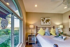 Relax in a serene bedroom with a large window overlooking lush greenery, a comfortable bed, and a bedside table with a lamp.