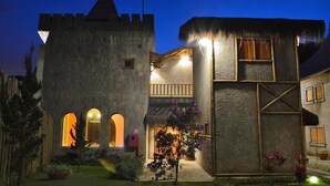 A castle-like building with a stone facade, arched windows, and a thatched roof. - Magique Le Canton (Teresópolis)