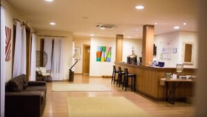 A hotel lobby with a reception desk, a seating area with a sofa and chairs, and a colorful abstract painting on the wall. - Magique Le Canton (Teresópolis)