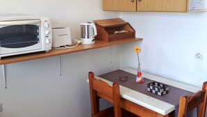 A compact kitchen with a microwave, toaster, kettle, and wooden cabinets. - Antzela Apartments (Corfu)