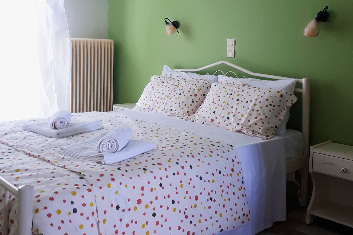 A neatly made bed with a polka dot bedspread, a bedside table, and a nightstand.