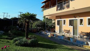 A two-story building with a balcony, outdoor seating, and a well-maintained garden. - Antzela Apartments (Corfu)