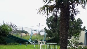 A garden with a palm tree, a swing set, and a bench. - Antzela Apartments (Corfu)