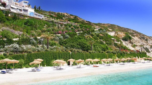 A beach with clear turquoise water, white sand, and a row of thatched umbrellas. - Seafront home 4' walk to private beach (Malevizi)