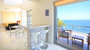 A modern hotel room with a balcony, a dining area, and a view of the sea. - Seafront home 4' walk to private beach (Malevizi)