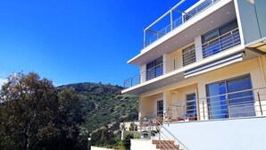 A modern two-story building with a balcony, large windows, and a staircase leading to the upper floor. - Seafront home 4' walk to private beach (Malevizi)