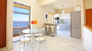 A modern kitchen with a view of the sea, a dining area with a glass table, and a bar. - Seafront home 4' walk to private beach (Malevizi)