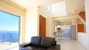 A modern living room with a glass coffee table, a leather sofa, and a view of the sea. - Seafront home 4' walk to private beach (Malevizi)