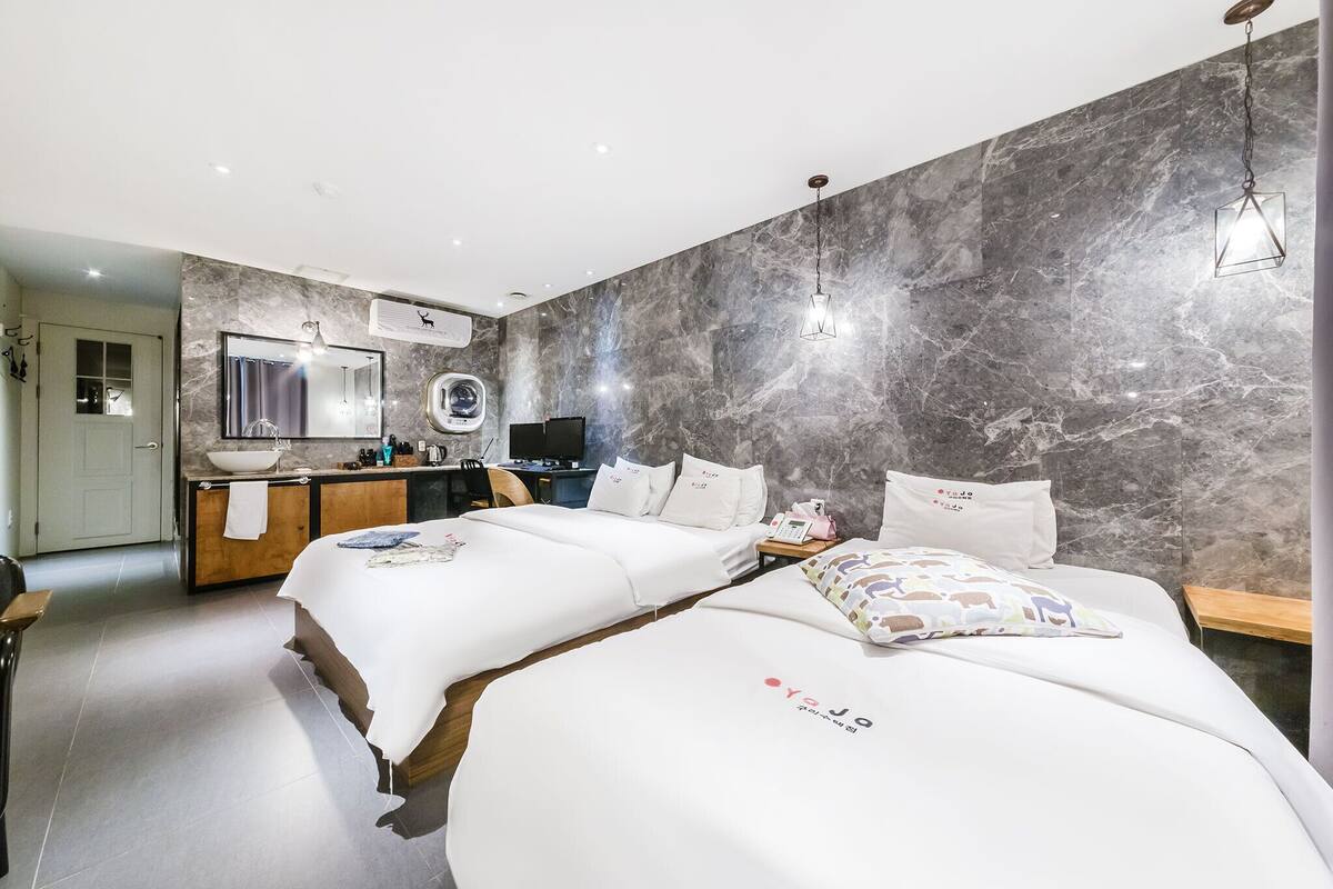 A modern hotel room with two beds, a vanity with a mirror, and a marble wall.