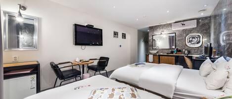 Une chambre d’hôtel comprenant un lit, un bureau avec une chaise, une télévision, un miroir et une petite kitchenette.