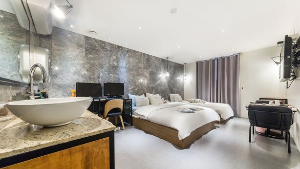 A modern hotel room with a large bed, a desk, a TV, and a bathroom with a sink and mirror.