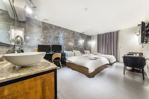 Una habitación de hotel moderna con una cama grande, un escritorio, un televisor y un baño con lavabo y espejo.