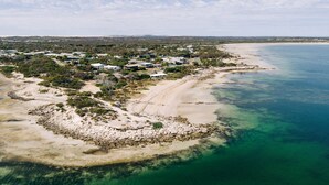 An aerial view of a coastal area with a beach, clear blue waters, and a cluster of buildings with a sandy shoreline.