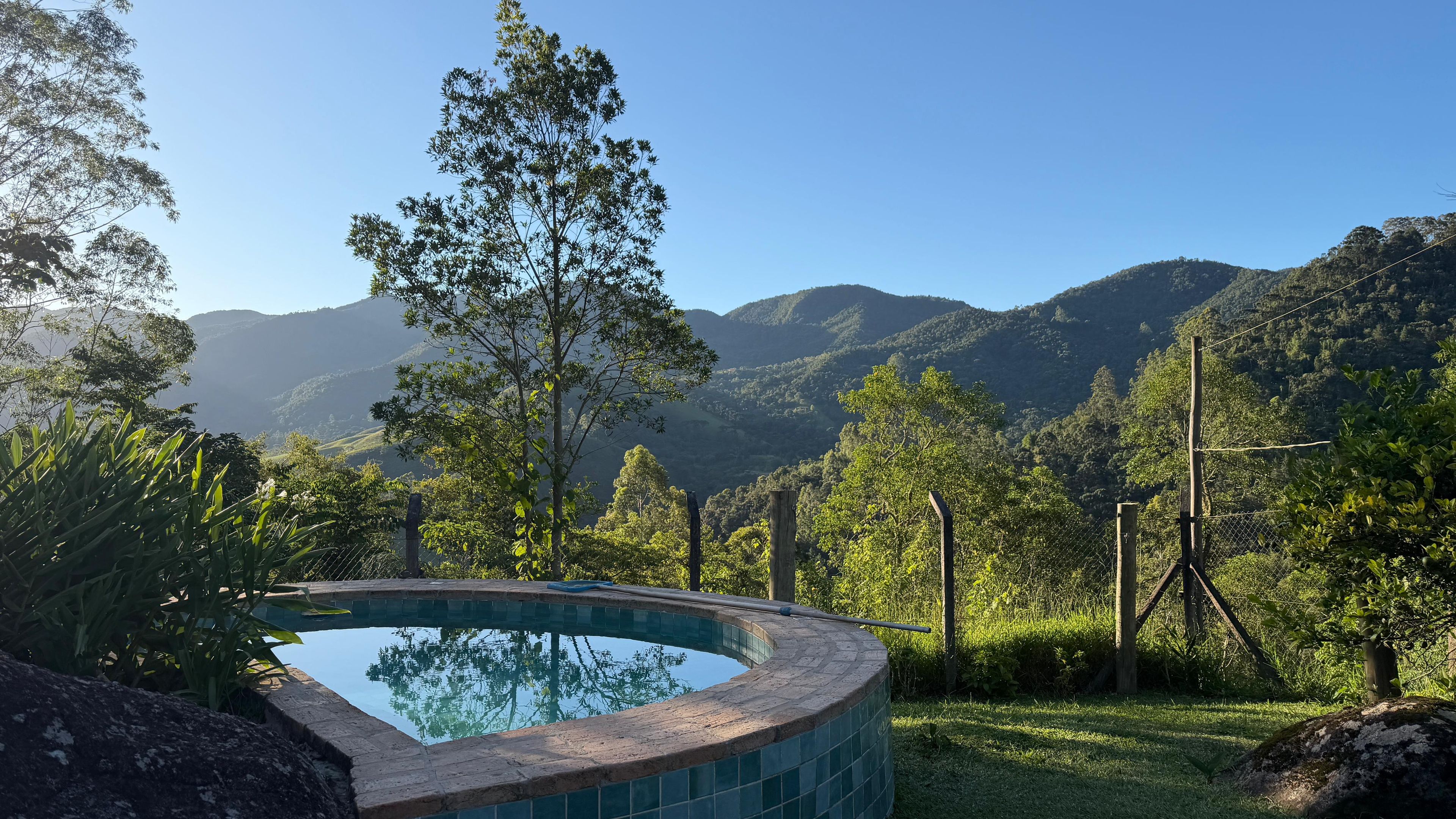 Une piscine à bord incurvé, entourée d’une végétation luxuriante et dominée par un paysage montagneux.