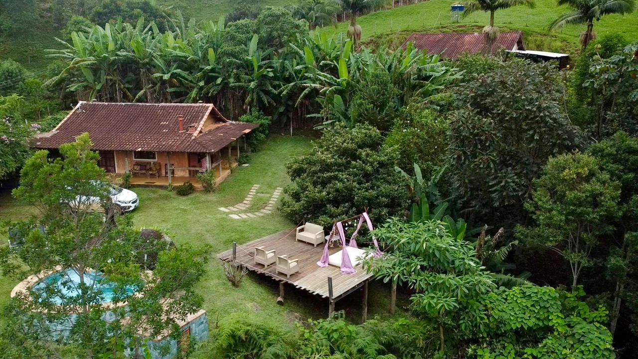 Une maison entourée d’une végétation luxuriante, dotée d’une terrasse en bois et d’un espace salon extérieur.