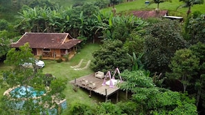 Une maison entourée d’une végétation luxuriante, dotée d’une terrasse en bois et d’un espace salon extérieur.