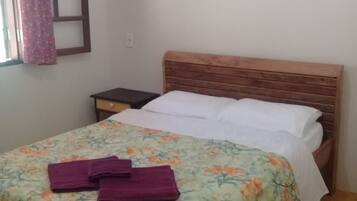Un letto singolo con copriletto floreale, una testiera in legno e un comodino con una lampada.