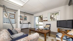 Ein Wohnzimmer mit einer Couch, einem Couchtisch und einem Fernseher. Es gibt eine Küchenzeile mit einer Arbeitsplatte und Schränken.