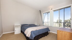 Ein Schlafzimmer mit Bett, Nachttisch, Kommode und einem großen Fenster mit Blick.