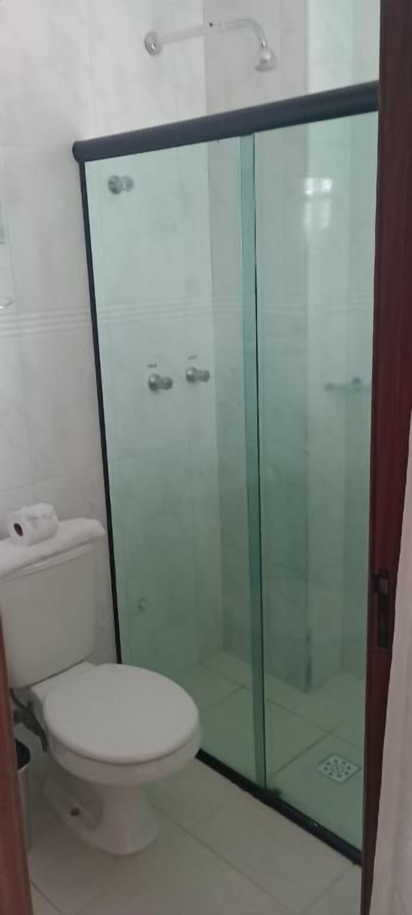 Un baño con ducha envuelta en vidrio, inodoro y lavamanos blanco.